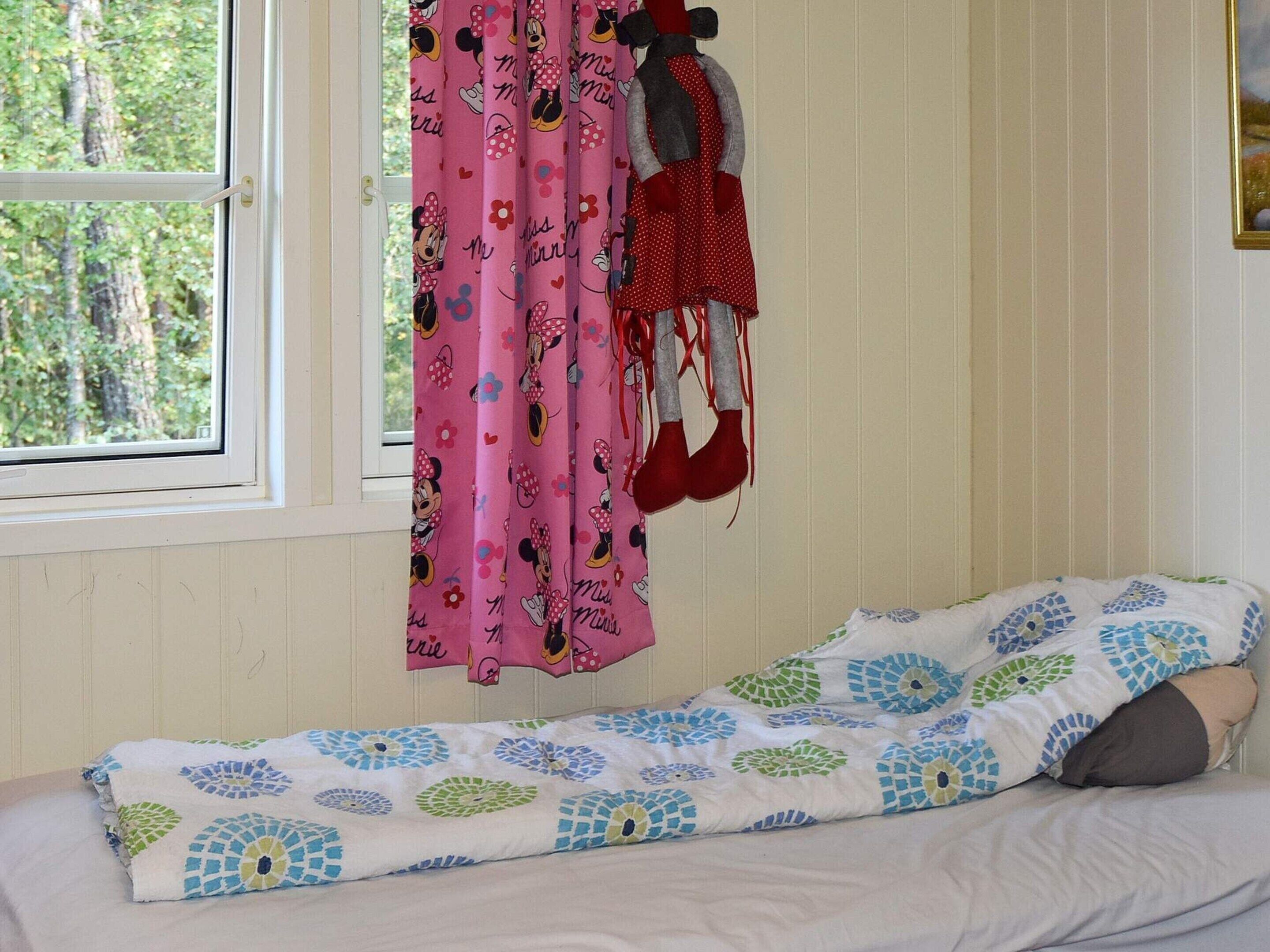 A room with a bed, a window with curtains, and a view of trees outside.