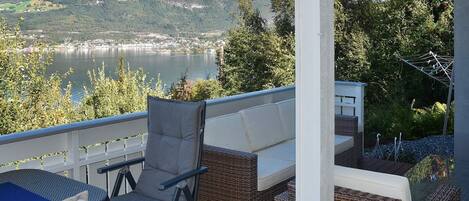 A balcony with wicker furniture, a view of a lake, and mountains in the background.