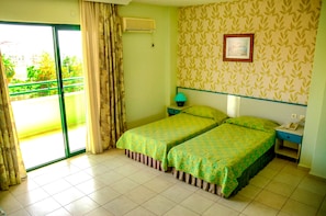 A room with two beds, a window with curtains, a wall-mounted air conditioner, a bedside table with a lamp, and a framed picture on the wall. - Green Park Apart Hotel (Alanya)