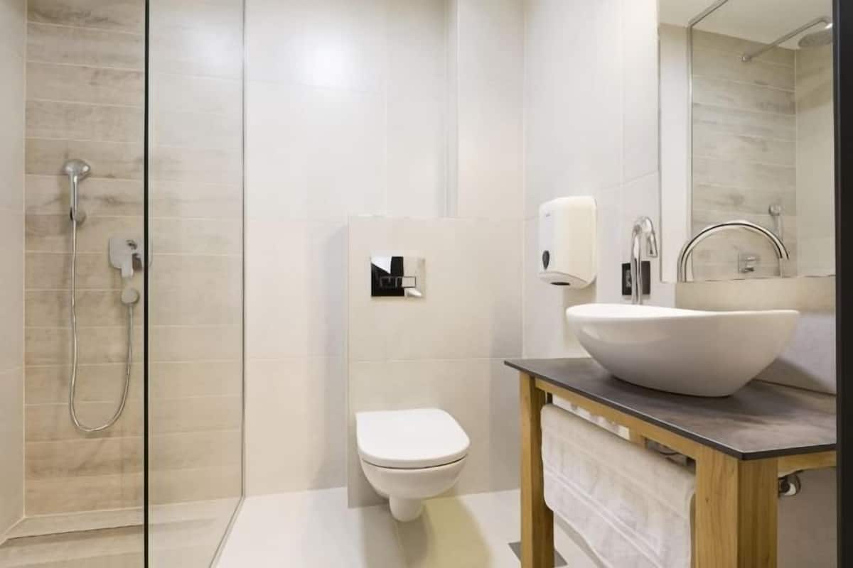 Une salle de bain moderne avec une douche à parois de verre, des toilettes blanches et un meuble-lavabo en bois doté d’un grand lavabo sur pied.