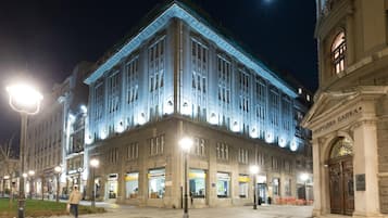 A large, multi-story building with a prominent corner entrance, illuminated by street lamps.