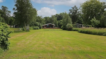 A grassy field with a wooden cabin and a smaller structure in the background.