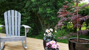 A wooden deck with a gray Adirondack chair and two potted plants with flowers. - 4 Star Holiday Home in Jaegerspris (Jægerspris)