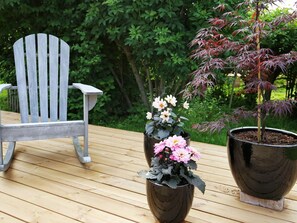 Una terraza de madera con una silla Adirondack gris y dos macetas con flores.