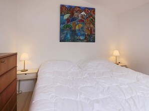 A bedroom with a bed, two bedside tables with lamps, a wooden dresser, and a painting on the wall. - 4 Star Holiday Home in Jaegerspris (Jægerspris)