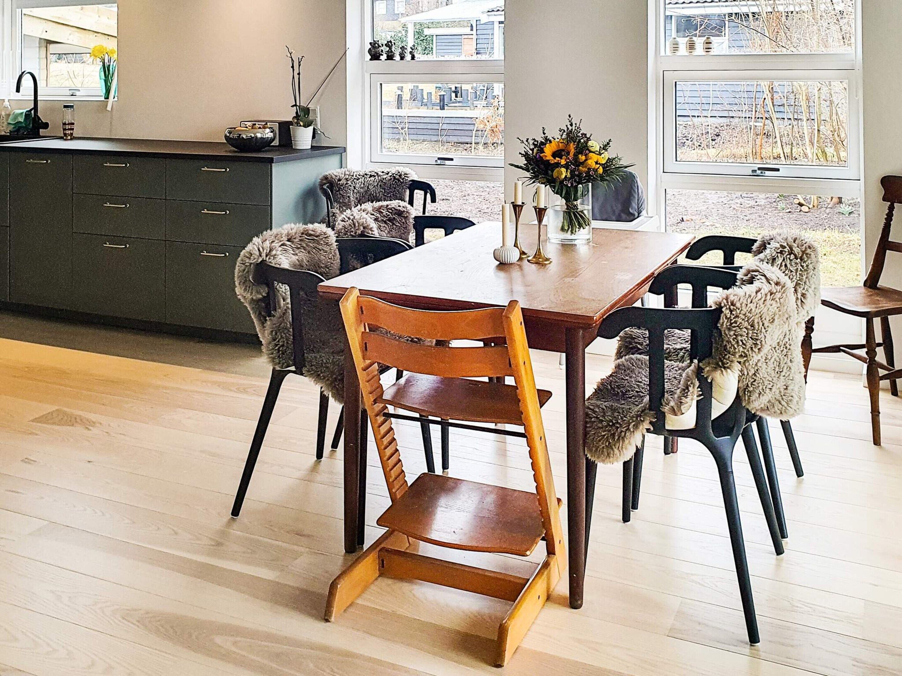 Ein Essbereich mit Holztisch und Stühlen, einer Vase mit Blumen und Blick durch große Fenster.