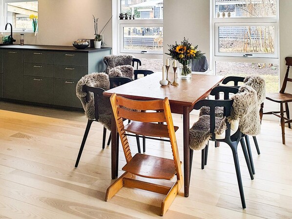 A dining area with a wooden table and chairs, a vase with flowers, and a view through large windows. - 4 Star Holiday Home in Jaegerspris (Jægerspris)
