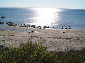 Una playa con barcos y gente, cielo despejado y mar tranquilo.