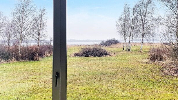 A view through a door into a grassy outdoor area with trees and a pile of branches. - 4 Star Holiday Home in Jaegerspris (Jægerspris)