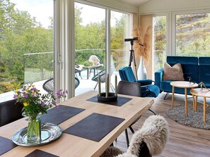 A modern interior with a wooden dining table, a sofa, and a balcony with a view of greenery. - 6 Person Holiday Home in Digermulen (Vagan)