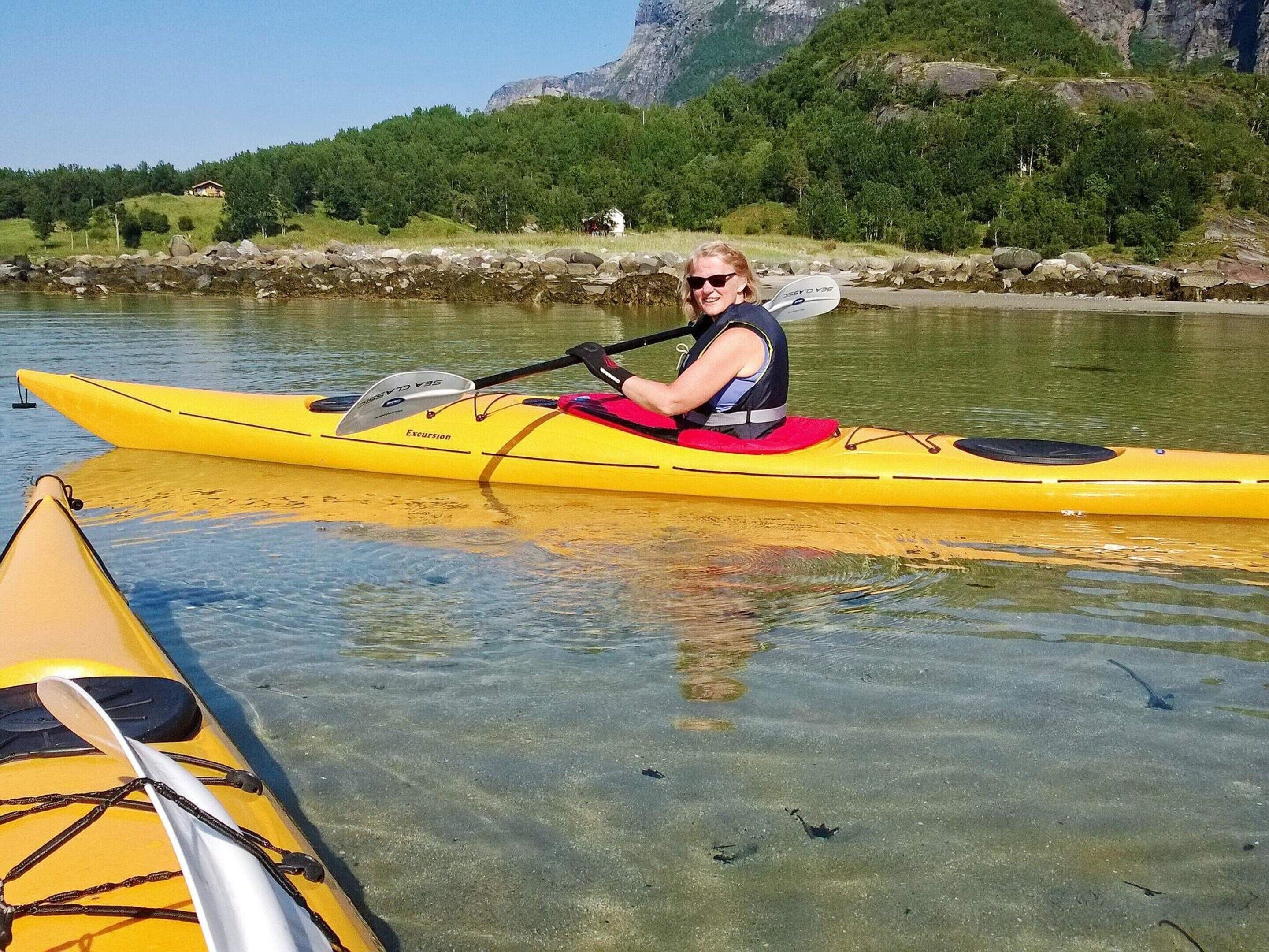 A person in a yellow kayak on a calm body of water with a rocky and forested shoreline in the background.