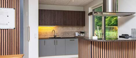 A modern kitchen with dark wooden cabinets, a stainless steel range hood, and a window with a view of greenery.