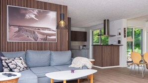 A modern living room with a grey sofa, a round white coffee table, and a wicker side table. A large framed picture of a beach scene is on the wall. - 6 Person Holiday Home in Juelsminde-by Traum (Horsens)