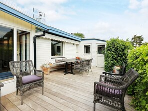 Een overdekt terras met een eettafel en stoelen, omringd door witte muren en een houten terras.
