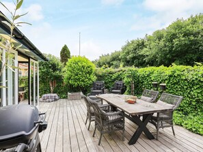 Een terras buiten met een houten terras, rieten meubels en een barbecue.