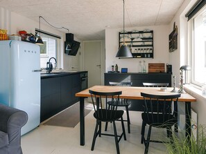 A compact kitchen with a blue refrigerator, black cabinets, and a dining area with a wooden table and black chairs.