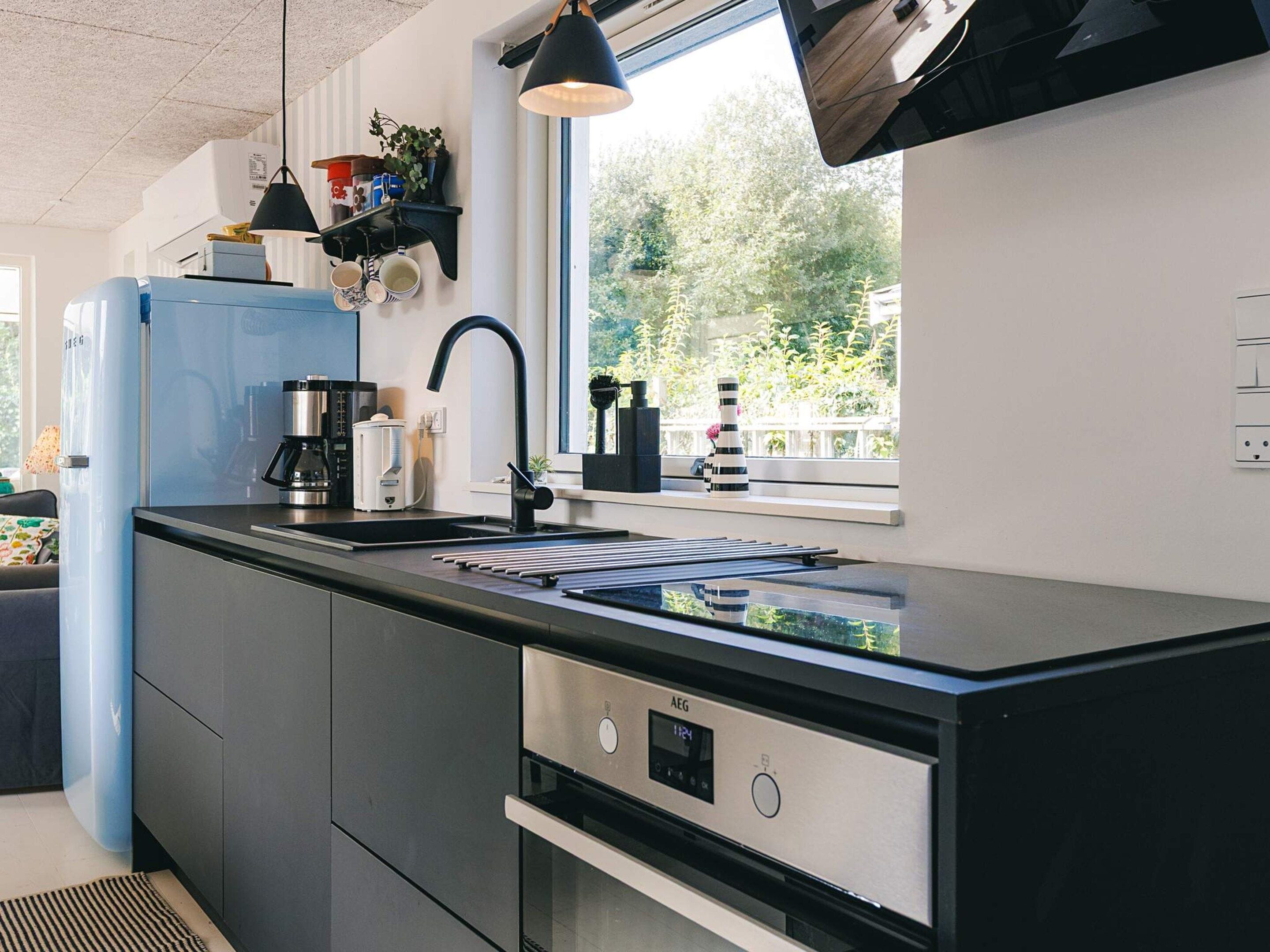 A modern kitchen with a black countertop, stainless steel appliances, and a window with a view of greenery.