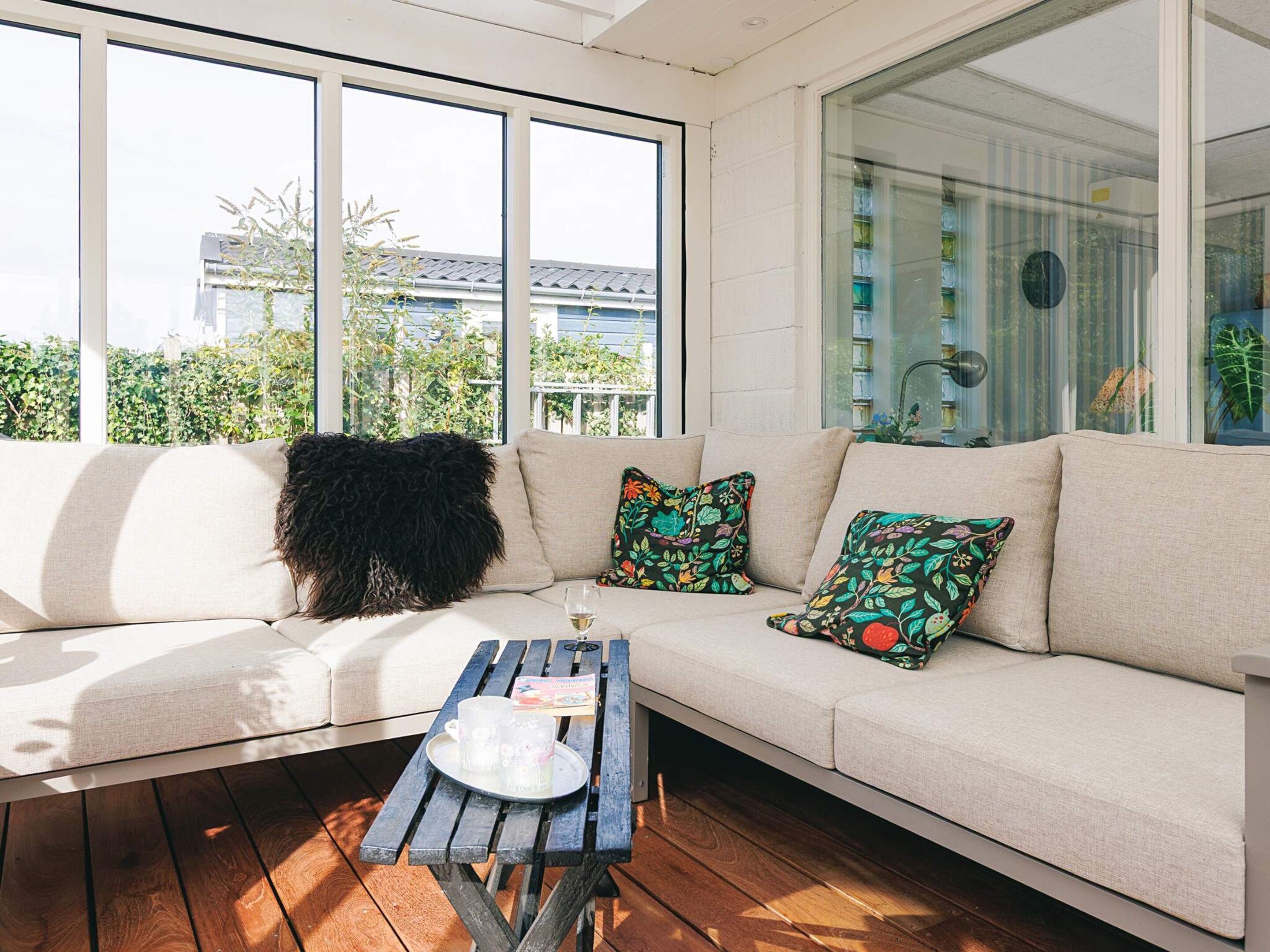 A sunlit room with a sofa, a wooden table, and a window with a view of greenery and buildings.