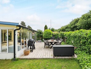 Een terras met buitenmeubilair, een barbecue en een glazen ruimte.