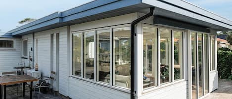 A covered patio area with a table and chairs, large windows, and a view of the backyard.