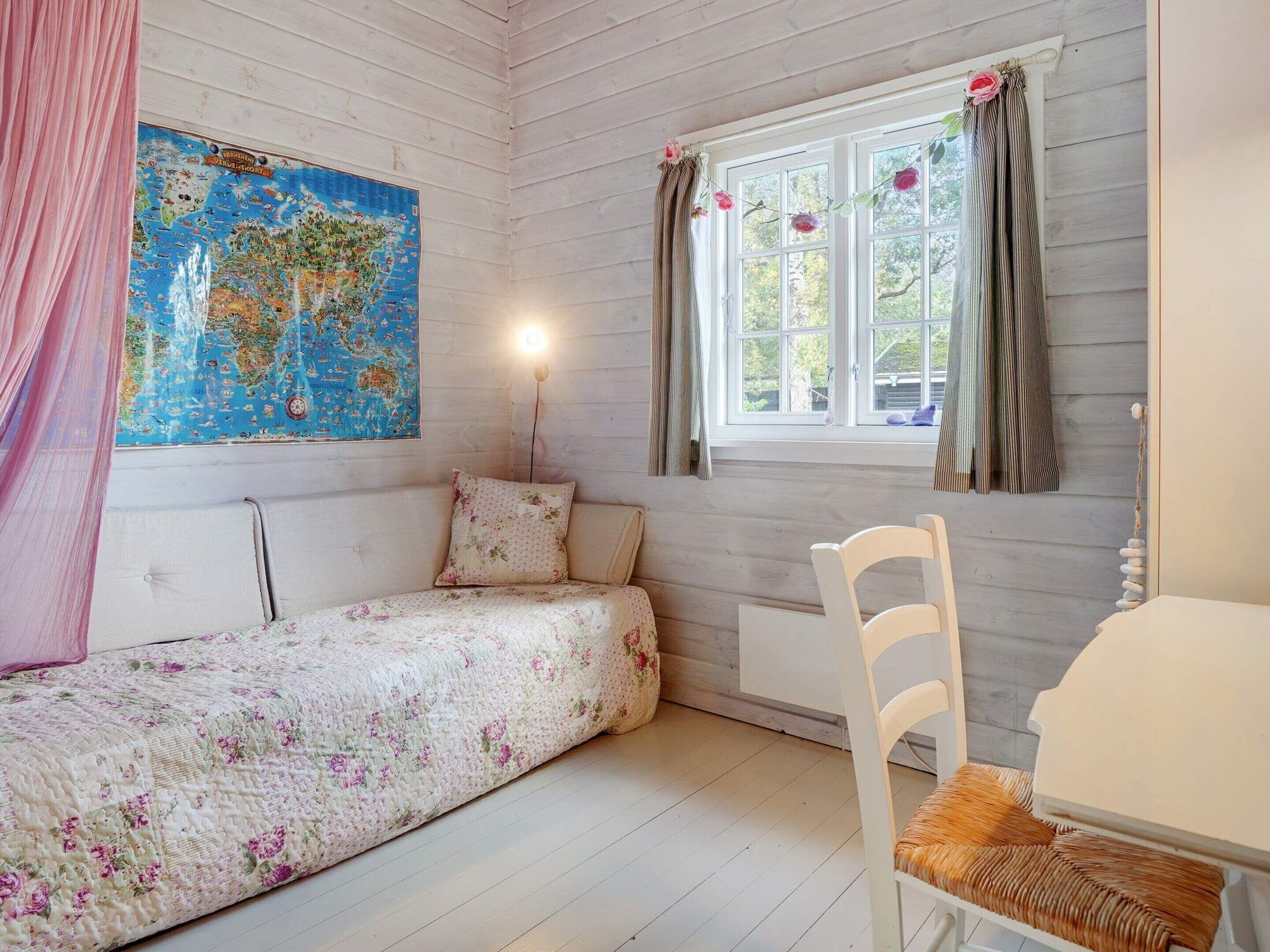 Une pièce confortable avec un lit, une chaise, une table, une carte accrochée au mur et une fenêtre avec des rideaux.
