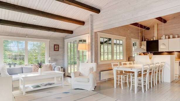 A spacious living room with a white sofa, a coffee table, and a dining area with a white table and chairs. Large windows allow natural light to fill the space. - 8 Person Holiday Home in Gilleleje (Gilleleje)
