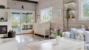 A spacious living room with a white sofa, a coffee table, and a fireplace. There is a large window providing natural light and a view of the outdoors. - 8 Person Holiday Home in Gilleleje (Gilleleje)