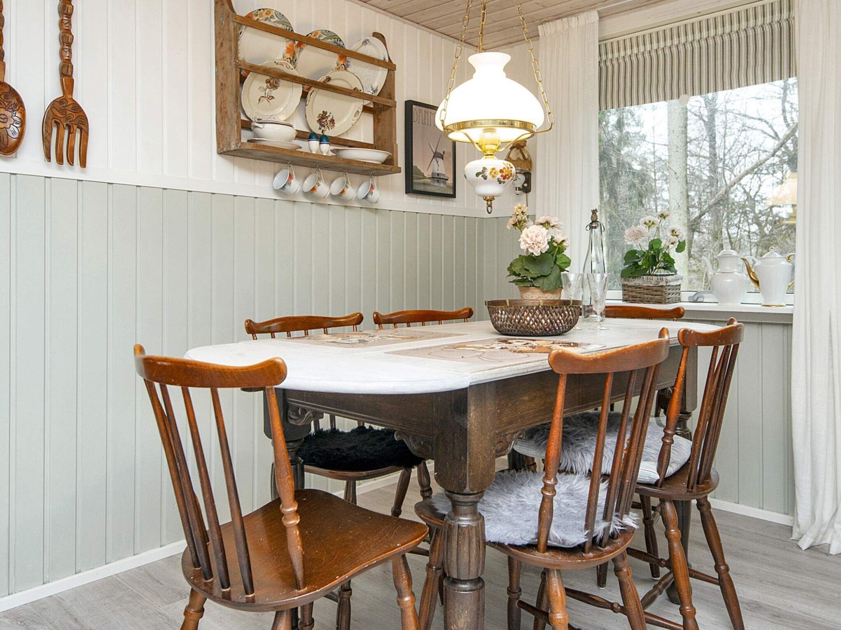 A dining area with a wooden table, six chairs, a chandelier, and a window with a view of trees.