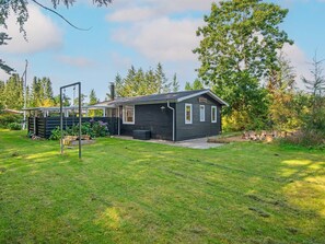 A small, dark-colored cabin with a porch and a swing set in a grassy yard.
