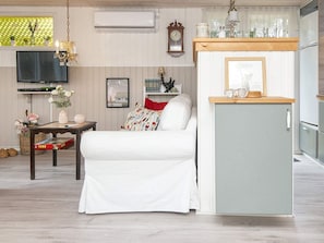 A compact living space with a white sofa, a small wooden table, a TV, and a kitchenette area with a refrigerator and a wooden countertop. - 4 Person Holiday Home in Glesborg (Glesborg)