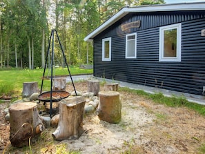 A cabin with a metal swing set and a fire pit area surrounded by tree stumps. - 4 Person Holiday Home in Glesborg (Glesborg)