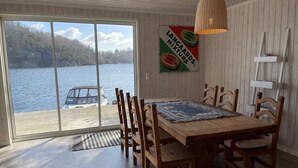 A dining area with a wooden table and chairs, a view of a lake with a boat, and a sign on the wall. - 6 Person Holiday Home in Rubbestadneset (Bomlo)