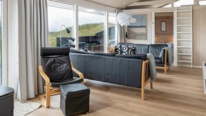 Een moderne woonkamer met een groot raam, een zwarte leren bank, een houten stoel en een klein pouf.