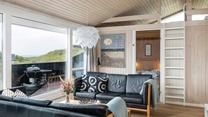Een moderne woonkamer met een zwarte leren bank, een houten salontafel en een groot raam met uitzicht op een grasveld.