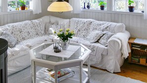 A cozy living room with a white floral sofa, a glass coffee table with a vase of flowers, and a bookshelf filled with books. - Holiday Home Near Kampinge Beach (Hollviken)