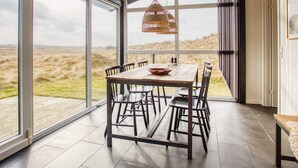 A dining area with a table and chairs, large windows, and a view of the outdoors.