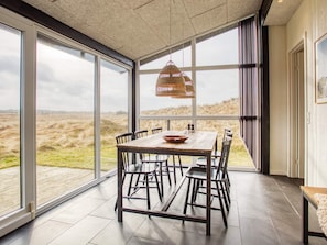 A dining area with a table and chairs, large windows, and a view of the outdoors.