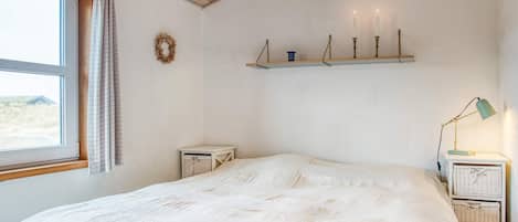 A bedroom with a large bed, a window with curtains, a shelf with candles, and a lamp on a bedside table.