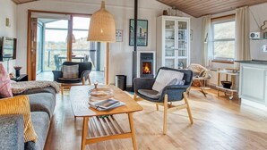 A spacious living room with a fireplace, wooden flooring, and a large window offering a view.