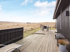 A wooden deck with a table and chairs, overlooking a grassy landscape.