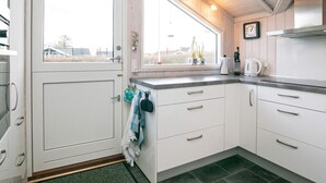 A modern kitchen with white cabinets, a window with a view, and a clock on the wall. - Tranquil Oasis in Blavand-by Traum (Rudkobing)