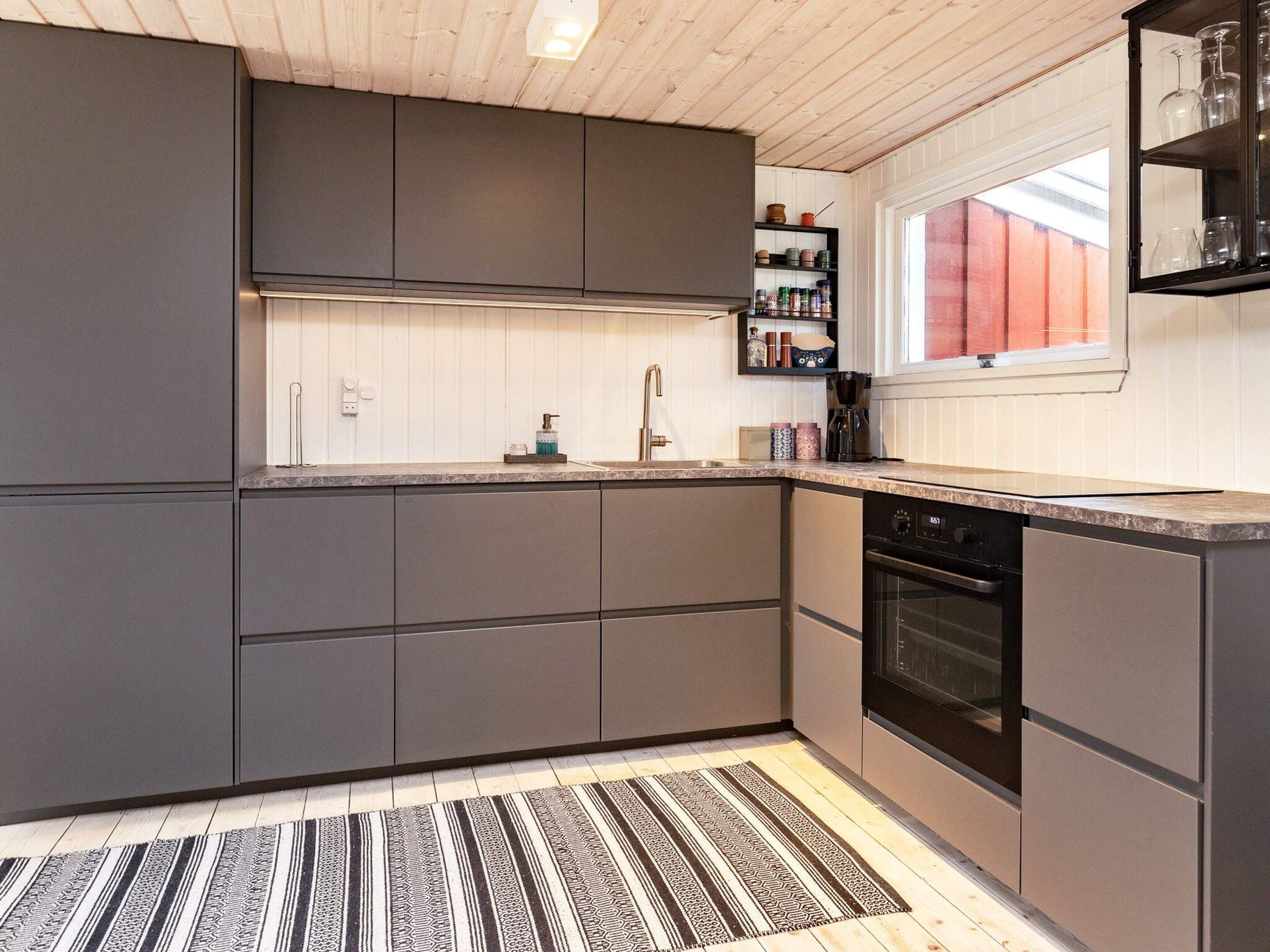A modern kitchen with grey cabinets, a built-in oven, and a window with a view.