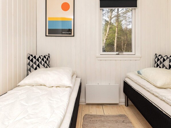 Une chambre avec deux lits, une fenêtre donnant sur la forêt et un tableau encadré accroché au mur.