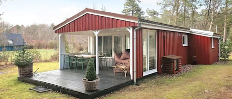 Una cabaña roja con un porche cubierto, un comedor con sillas y un pequeño jardín.