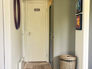 Un couloir avec une porte fermée, un panier en osier et deux œuvres d’art encadrées accrochées au mur.