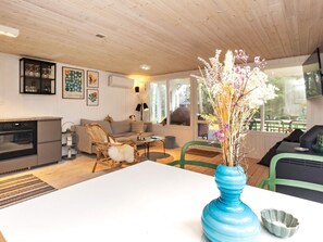 Un salon moderne avec une table blanche, un vase bleu orné de fleurs et un coin cuisine équipé d’une cuisinière.