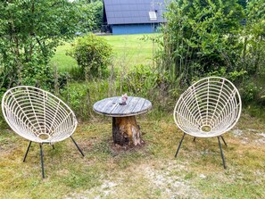 Un espace extérieur aménagé dans un style rustique, avec une table ronde en bois et deux chaises en osier.