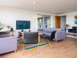 A modern living room with a sofa, chairs, a TV, and a dining area. - 5 Star Holiday Home in Ebeltoft (Ebeltoft)