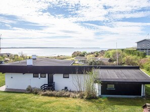 A modern house with a flat roof, a small porch, and a view of the sea.
