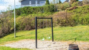 A playground with a swing set and a sandpit, surrounded by grass and bushes, with houses in the background. - 5 Star Holiday Home in Ebeltoft (Ebeltoft)